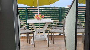 An open sliding glass door leading to an outdoor patio with a white table, chairs, and a fruit bowl. - Apartments Mlikota (Nin)