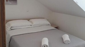 A single bed with a grey bedspread and two rolled towels. - Apartments Mlikota (Nin)