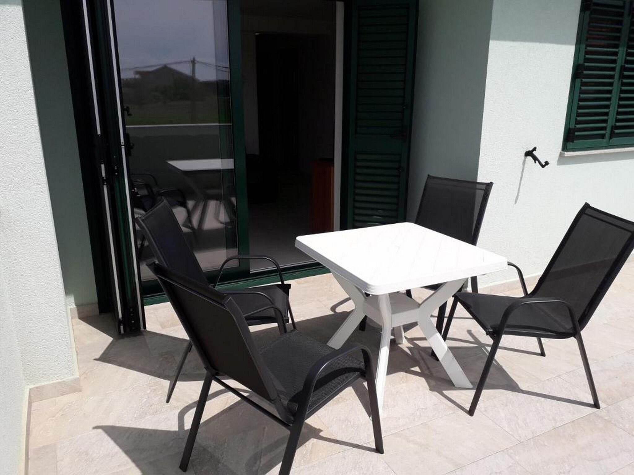Eine Terrasse im Freien mit einem weißen Tisch und vier schwarzen Stühlen.