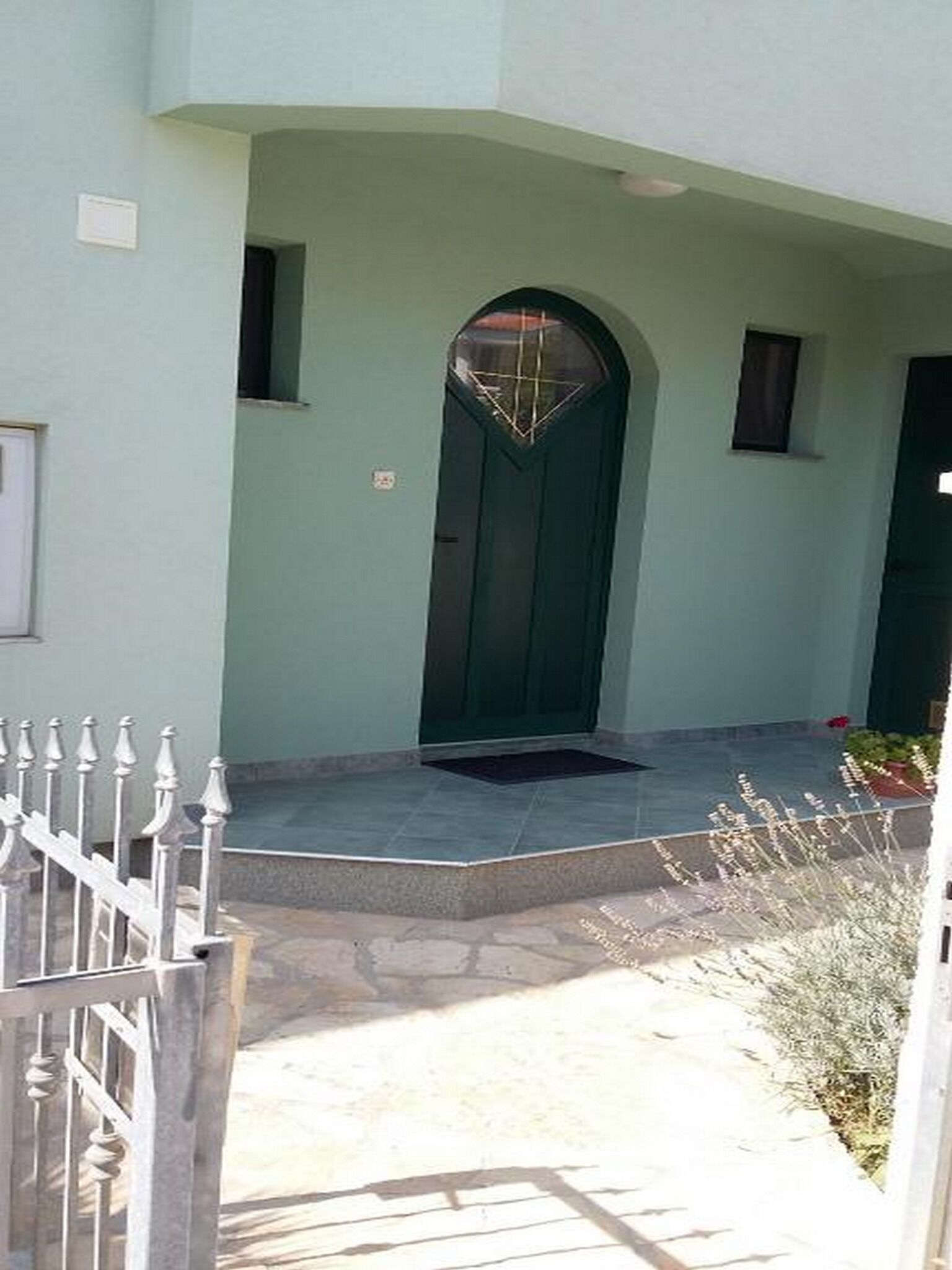 A building with a green door, a small window, and a white fence.