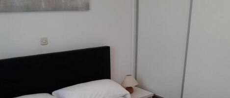 A neatly made bed with white linens and two rolled towels.