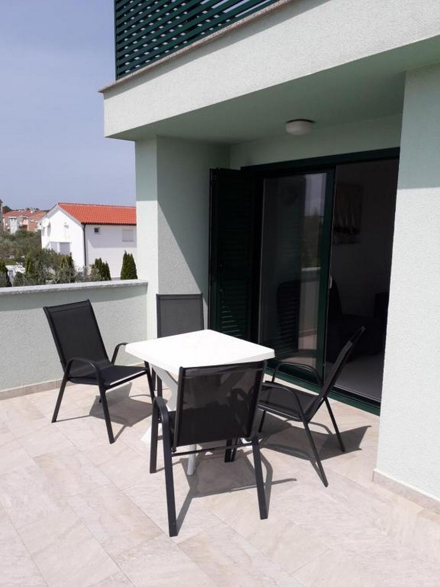 Ein Balkon mit einem weißen Tisch und vier Stühlen, einer Schiebetür und Blick auf benachbarte Gebäude.