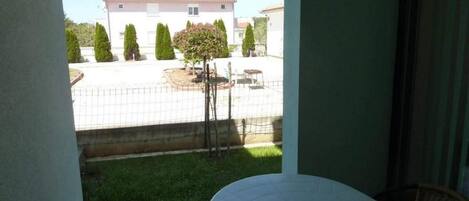 A balcony with a table and chairs, overlooking a fenced yard with a building and trees.