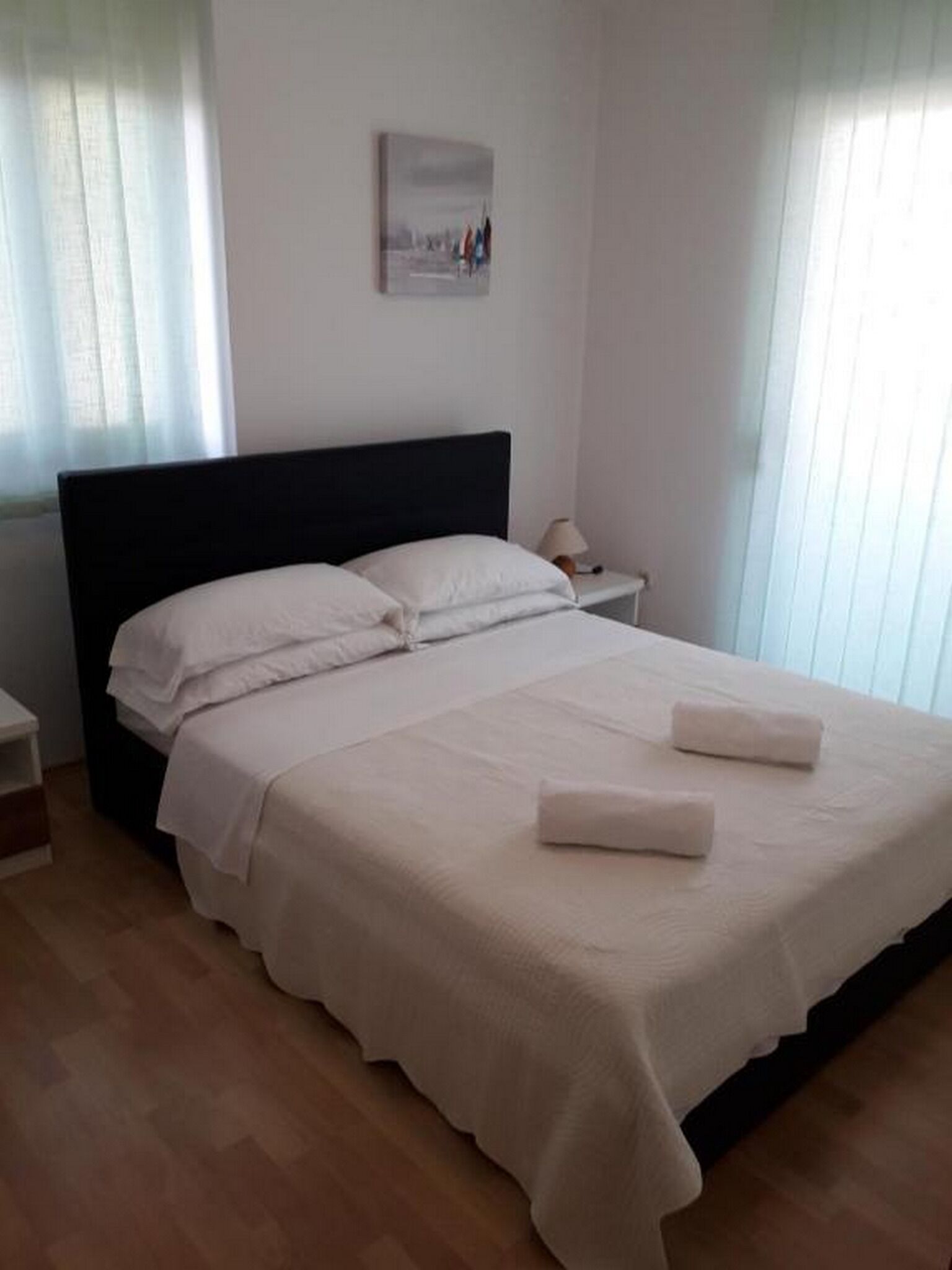 A neatly made bed with white linens and two folded towels, a bedside lamp, and a framed picture on the wall.