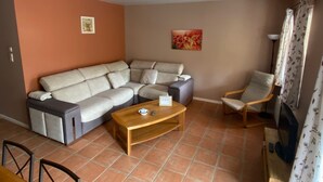Ein Wohnzimmer mit einem Ecksofa, einem Holztisch, einem Sessel und einem Gemälde an der Wand.