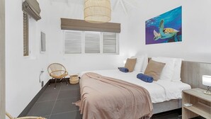 Een slaapkamer met een bed, een raam, een aan de muur bevestigd kunstwerk, een geweven lamp en een rieten stoel.