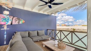 Een overdekt terras met een blauwe muur, een plafondventilator en uitzicht op het strand.