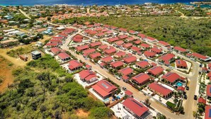 A residential area with multiple red-roofed houses arranged in a grid pattern, surrounded by greenery and a coastline. - Villa Kas Gia with garden and lovely private pool (Kralendijk)