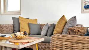 A wicker sofa with multiple cushions in a neutral color palette, a woven basket on a table, and a framed picture on the wall. - Villa Kas Gia with garden and lovely private pool (Kralendijk)
