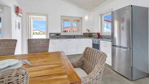 A modern kitchen with white cabinets, a stainless steel refrigerator, wicker chairs, and a wooden dining table. - Villa Kas Gia with garden and lovely private pool (Kralendijk)