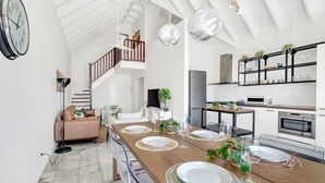 Een ruime woonkamer met een hoge plafond, een eettafel voor zes personen en een keuken met moderne apparatuur.