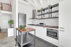 Une cuisine moderne avec des meubles blancs, un réfrigérateur en acier inoxydable, un four encastré et une table en bois agrémentée de plantes en pot.