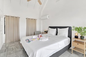 A hotel room with a bed, a bedside table with a lamp, a potted plant, and a window with curtains.