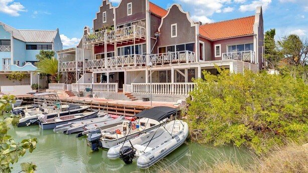 Een pand aan het water met een groot huis, meerdere balkons en een steiger met verschillende boten.