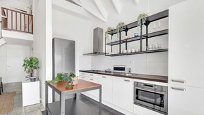 Een moderne keuken met witte kasten, een roestvrijstalen koelkast, een ingebouwde oven en een metalen schapunit in het zwart met planten.