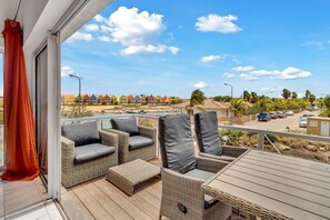 Un balcon doté de meubles en osier et offrant une vue sur une zone côtière, avec des maisons et des palmiers.