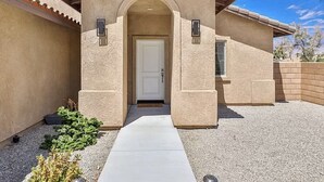 Una casa de un solo piso con fachada de estuco color beige, una puerta blanca y un ventanal pequeño.