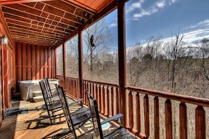 A wooden deck with a hot tub, rocking chairs, and a view of a forest. - Moonlight Ridge #2632 (Sevierville)