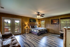 Un dormitorio con cama, paredes de madera, ventilador de techo y dos ventanas.