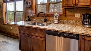 Una cocina con encimeras de granito, electrodomésticos de acero inoxidable, armarios de madera y una cafetera.