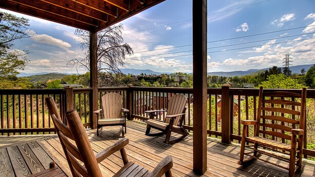 Una terraza de madera con sillas y un banco, con vistas a un paisaje pintoresco con montañas y árboles.