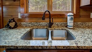 Una cocina con encimera de granito, un lavamanos doble y una ventana con vistas a árboles.
