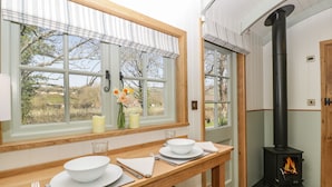 A kitchen with a wooden table set for dining, a window with curtains, and a wood-burning stove.