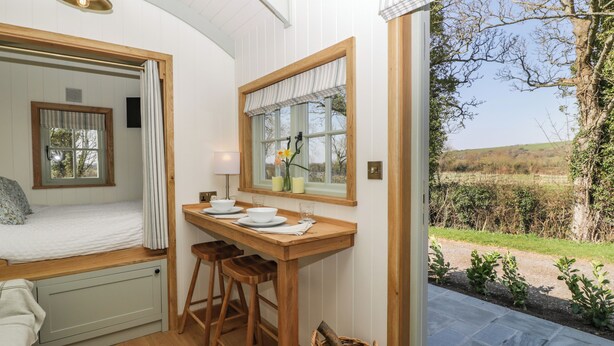 A cozy room with a bed, a small table with stools, a window with curtains, and a view of the outdoors.
