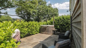 Un patio exterior con un jacuzzi, muebles de mimbre y vistas a un paisaje arbolado.