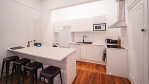 A compact kitchen with white cabinetry, a microwave, a sink, and a small island with stools. - Refurbished Villa  ✨ NEW ✨ Hot tub, Netflix, & Entirely private (Hastings)