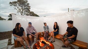 A group of people sitting around a fire pit in an outdoor patio area with string lights.