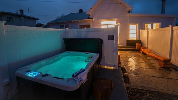 A hot tub in a backyard with a wooden fence, a bench, and a house in the background. - Refurbished Villa  ✨ NEW ✨ Hot tub, Netflix, & Entirely private (Hastings)