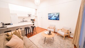 A modern living room with a sofa, coffee table, and two armchairs. A kitchen area with white cabinets and a microwave is visible in the background. - Refurbished Villa  ✨ NEW ✨ Hot tub, Netflix, & Entirely private (Hastings)