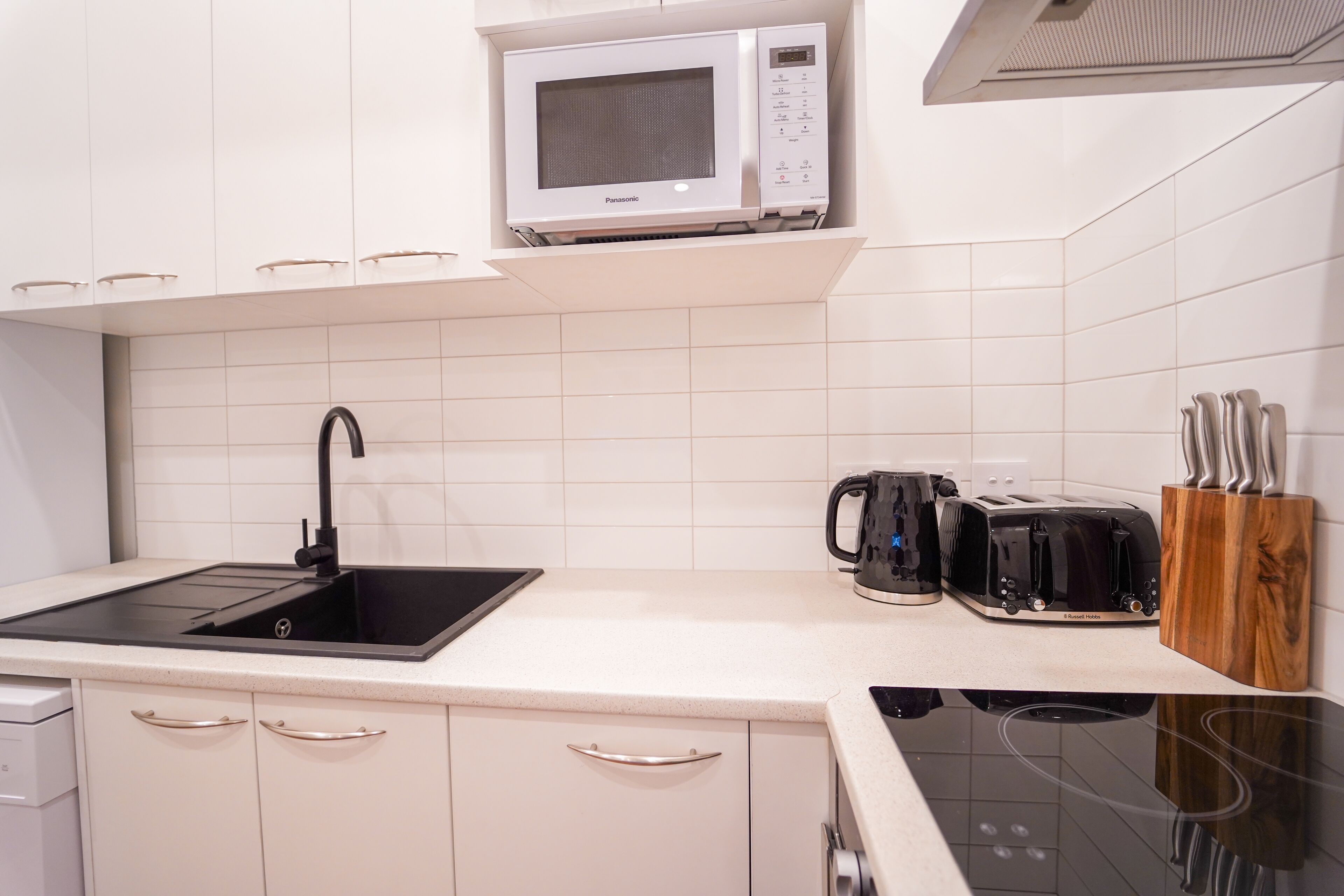 A modern kitchen with white cabinetry, a black sink, a microwave, a toaster, and a coffee maker.