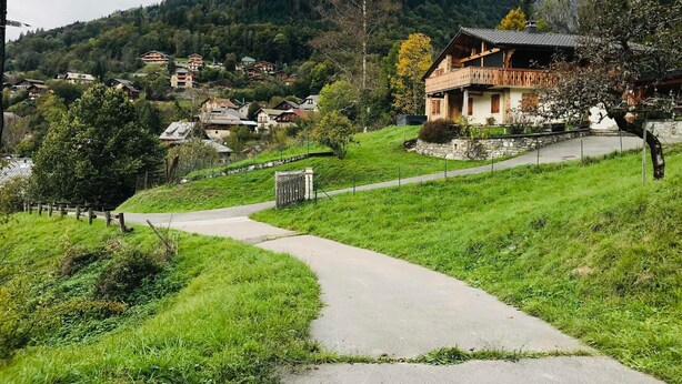 Un village rural, avec une route sinueuse menant à un chalet traditionnel doté d’un balcon.