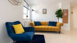 Ein modernes Wohnzimmer mit einem blauen Sessel, einem gelben Sofa und einem großen Fenster mit Jalousien.