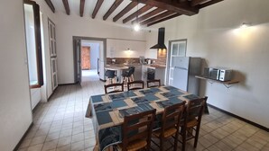 A dining area with a table set for four, wooden chairs, a kitchen in the background, and a ceiling with exposed beams. - Charming Farmhouse Retreat with Enclosed Garden, A/C, and Farm Tours in Berry (Cluis)