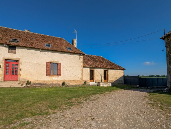 A rustic stone building with a red door and a small garden area in front.