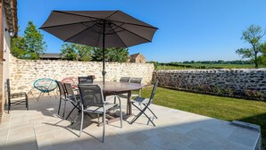 An outdoor patio with a stone wall, a table with chairs, and an umbrella. - Charming Farmhouse Retreat with Enclosed Garden, A/C, and Farm Tours in Berry (Cluis)