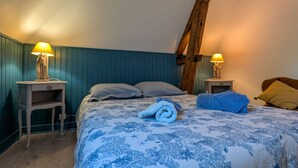 A bedroom with a bed, two bedside tables with lamps, a wooden beam, and a blue floral bedspread. - Charming Farmhouse Retreat with Enclosed Garden, A/C, and Farm Tours in Berry (Cluis)