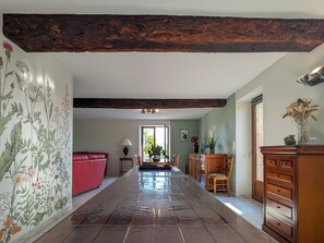 Un hall d’entrée spacieux avec un plafond en bois, un canapé rouge, une table à manger avec des chaises et un buffet en bois.