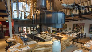 Een modern restaurant met een centraal gelegen bar, meerdere eettafels en een unieke plafondsculptuur.