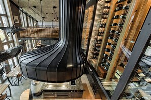 A modern interior with a central black structure, wooden shelves with wine bottles, and a dining area with tables and chairs. - Lartor Resort (Unterammergau)