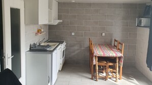A compact kitchen with white cabinets, a built-in oven, and a microwave. There's a dining table with chairs and a patterned tablecloth. - Rental T1 30m2 with Terrace in Brem Sur Mer: 2km from the beach (Brem-sur-Mer)