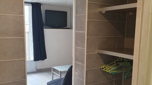 A room with a TV mounted on the wall, a chair, a small table, and a shelf with hangers. - Rental T1 30m2 with Terrace in Brem Sur Mer: 2km from the beach (Brem-sur-Mer)