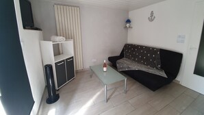 A living room with a sofa, a coffee table, a TV, a radiator, and a shelf with towels. - Rental T1 30m2 with Terrace in Brem Sur Mer: 2km from the beach (Brem-sur-Mer)