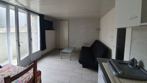 A compact living space with a dining table, a sofa, a small table, and a kitchen area with a microwave. - Rental T1 30m2 with Terrace in Brem Sur Mer: 2km from the beach (Brem-sur-Mer)