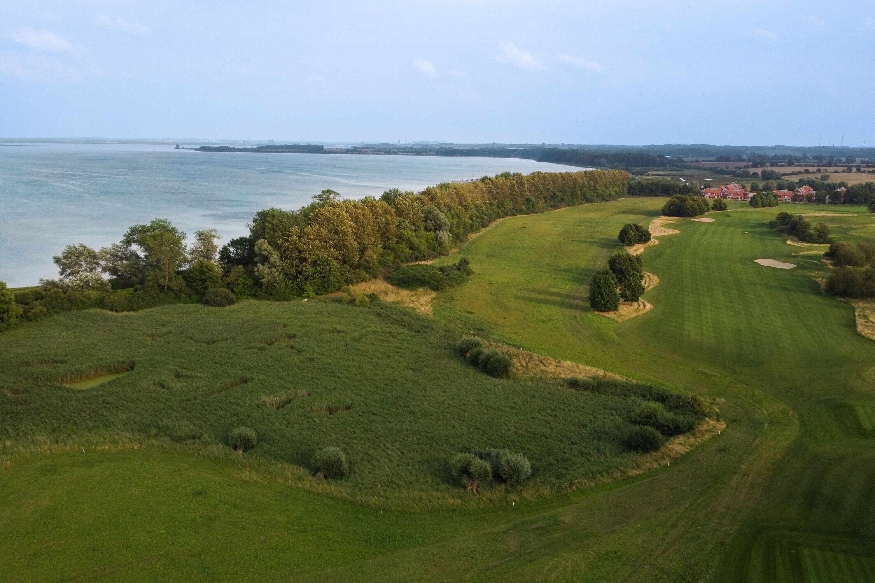 Um campo de golfe com vista para o mar e edifícios ao longe.