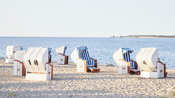 Strandliegen mit Nummern, auf einem sandigen Strand aufgereiht, mit dem Meer im Hintergrund.