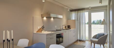 A modern kitchen with a dining area, featuring a built-in oven, a coffee maker, and a window with curtains.